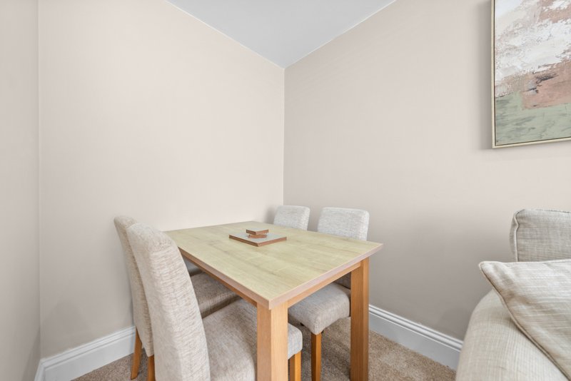 Compact dining area with wooden table, upholstered chairs and framed artwork on wall