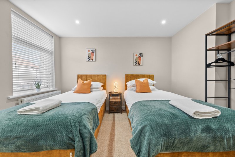 Twin bedroom with two single beds, teal blankets, orange headboards and modern shelving unit