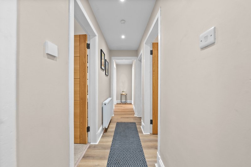 Modern hallway with wooden doors, light wood flooring, runner rug and recessed lighting
