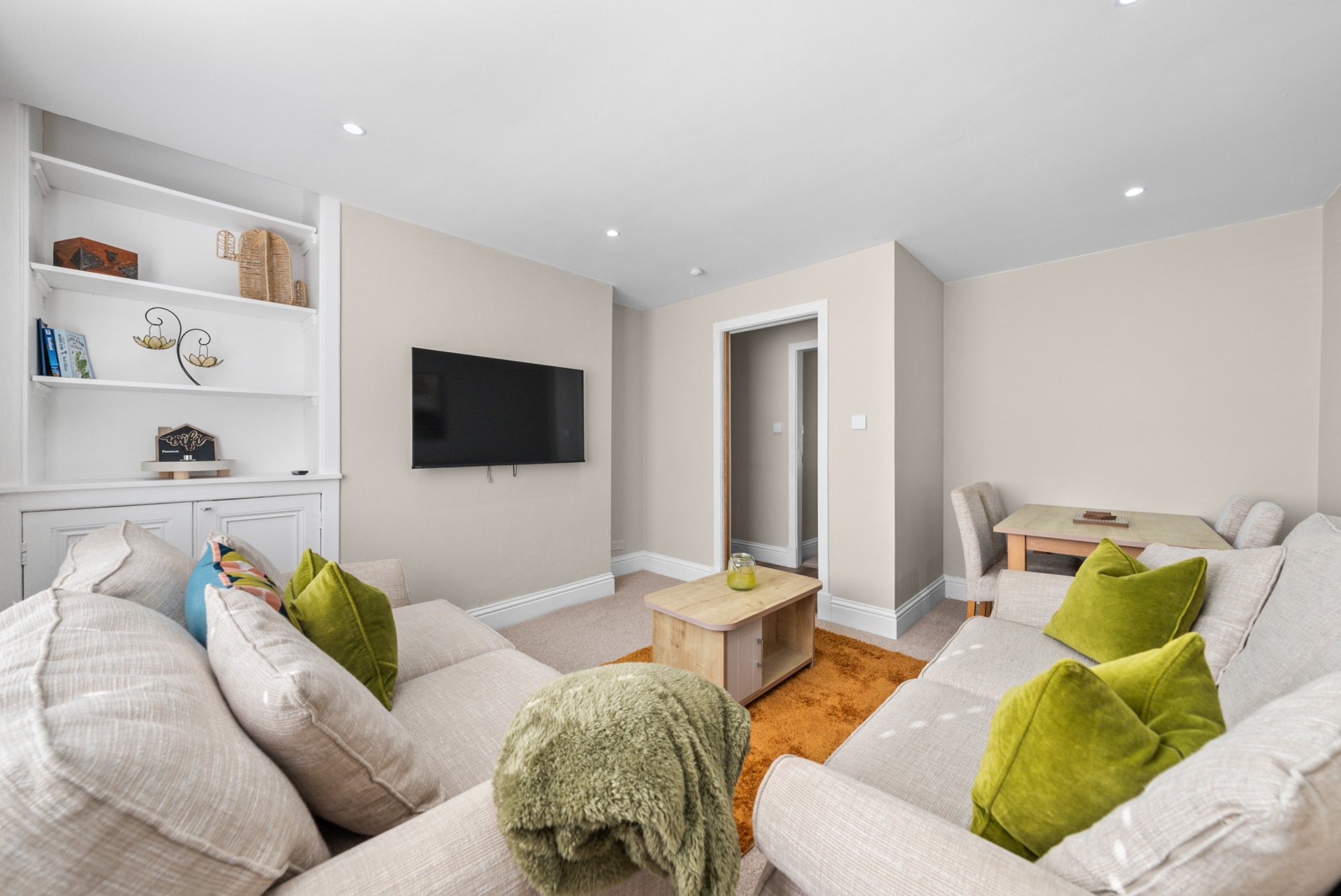 Modern living room with two white sofas, green cushions, mounted TV, and built-in shelving