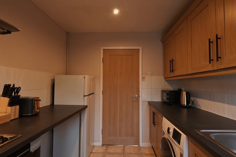 Galley kitchen with wooden cabinets, black countertops, stainless steel appliances and tile flooring