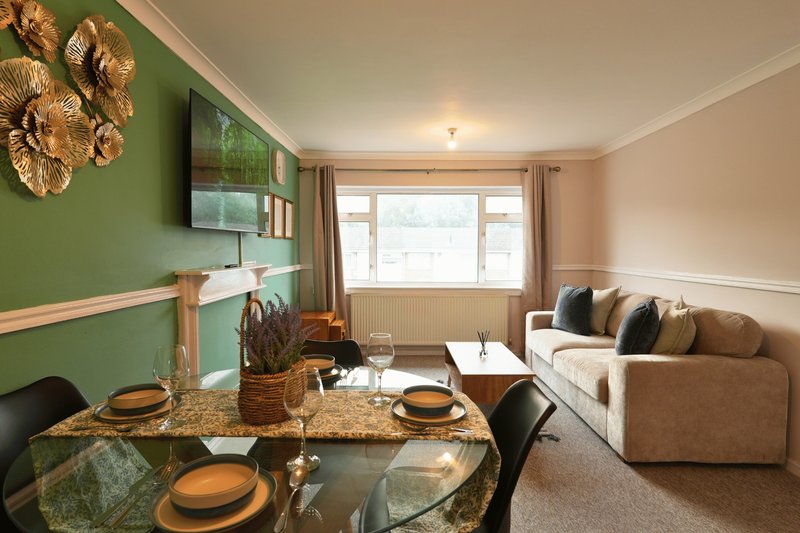 Open-plan living and dining room with green accent wall, sofa, and dining table set for four