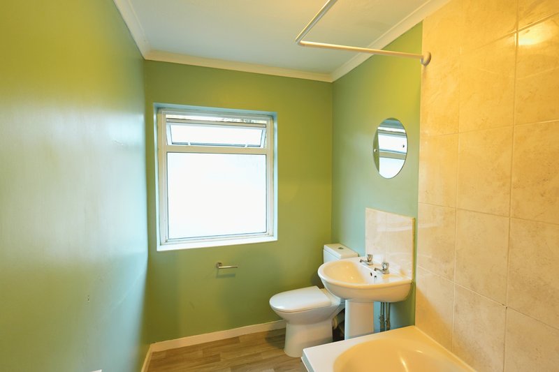 Bathroom with green walls, pedestal sink, toilet, window and yellow bathtub