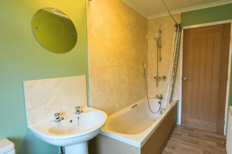 Bathroom with pedestal sink, bath with shower enclosure, green walls and round mirror