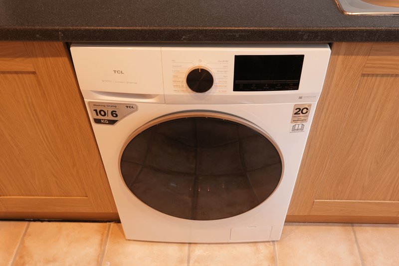 White front-loading washing machine with digital display built into wooden kitchen cabinetry