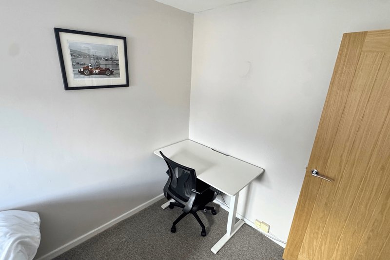 Compact home office with white desk, black chair, framed picture and wooden door