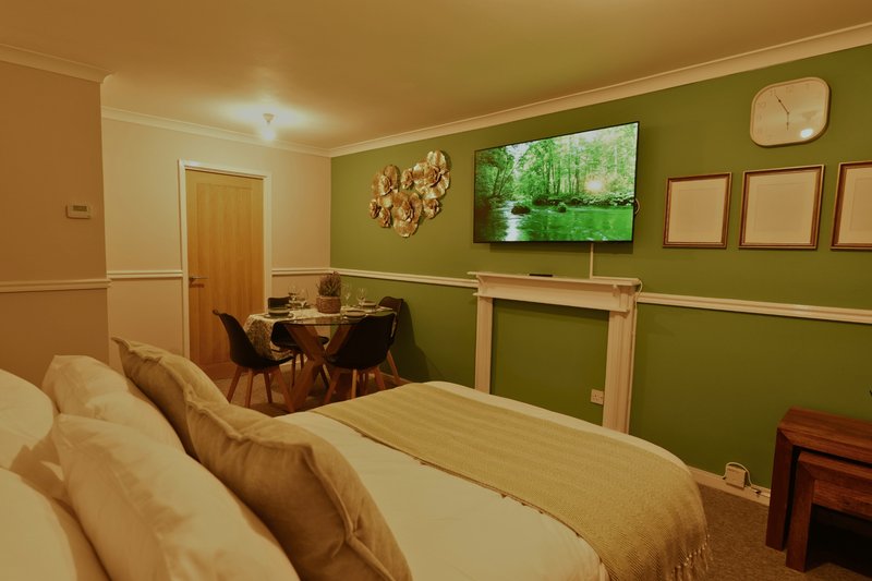 Bedroom with double bed, work desk, green accent wall and wall-mounted TV