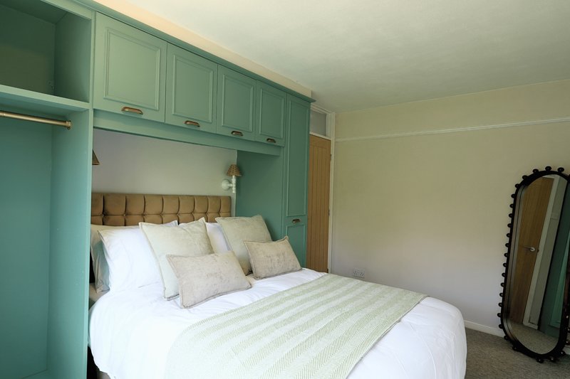 Bedroom with double bed, green built-in wardrobes, beige headboard and round mirror