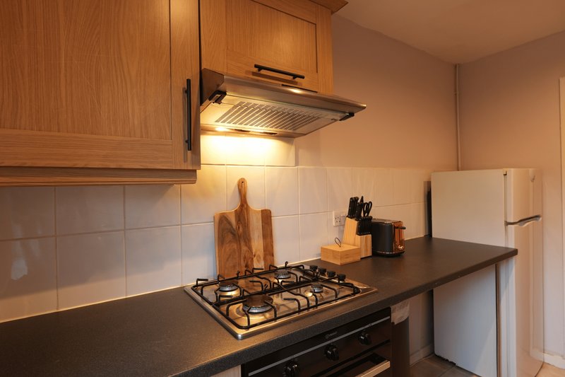 Kitchen with gas hob, wooden cabinets, white tiled backsplash and black countertop