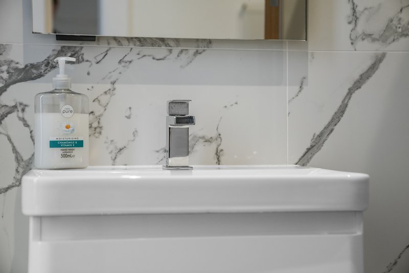 Modern bathroom sink with marble splashback, chrome tap and hand soap dispenser