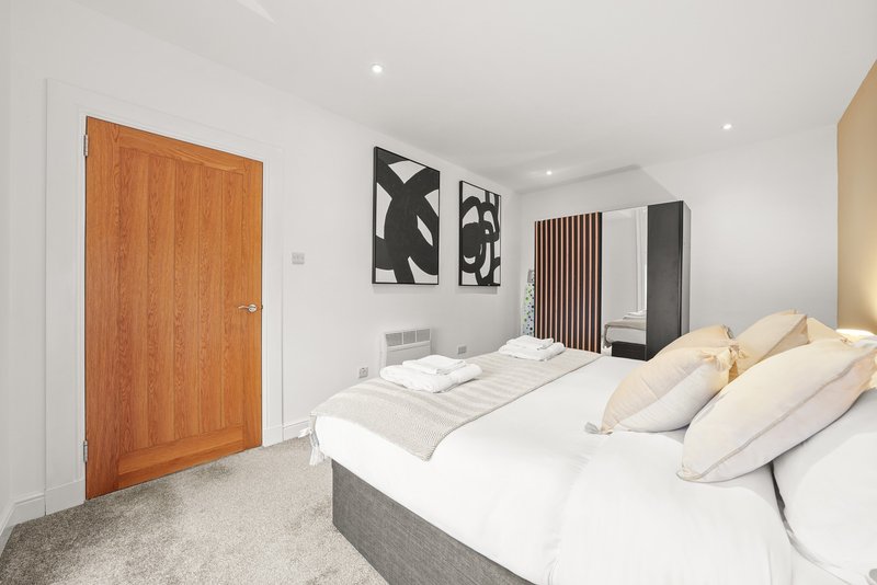 Modern bedroom with double bed, cream pillows, wooden door and black wall art