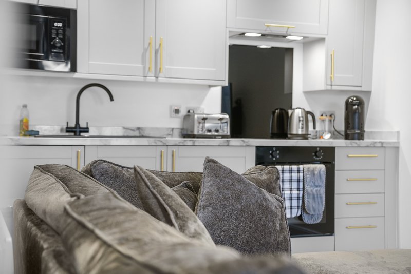 Modern kitchen with white cabinetry, stainless steel appliances, and gray cushions in foreground