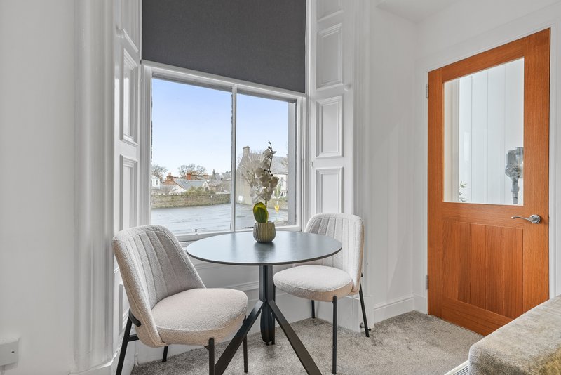 Bright corner room with round black table, two upholstered chairs, and large window overlooking garden