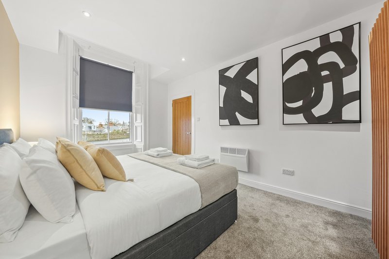Modern bedroom with double bed, yellow cushions, abstract wall art and city view