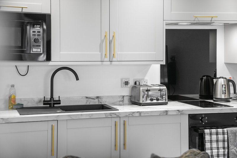 Modern white kitchen with black countertop, sink, microwave, kettle and toaster