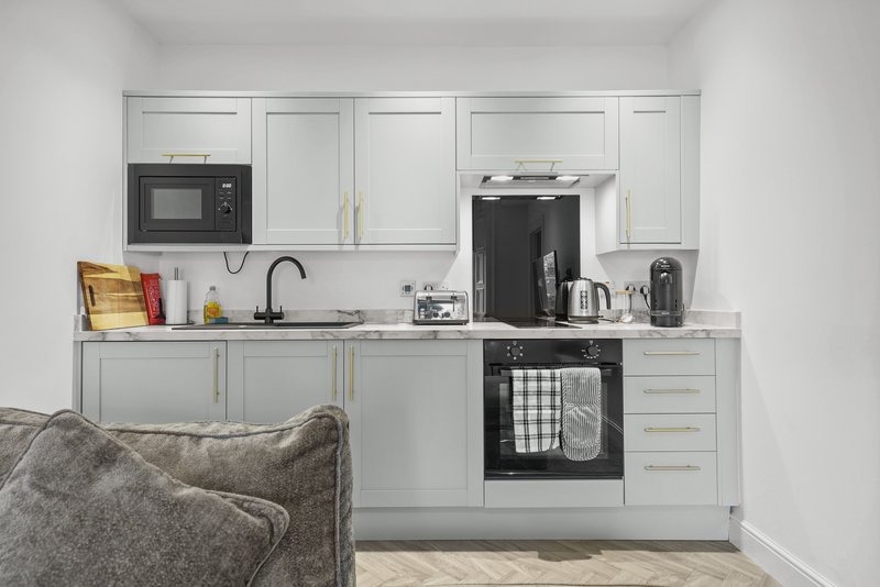 Modern kitchen with white cabinetry, black oven, sink, and various small appliances on countertop