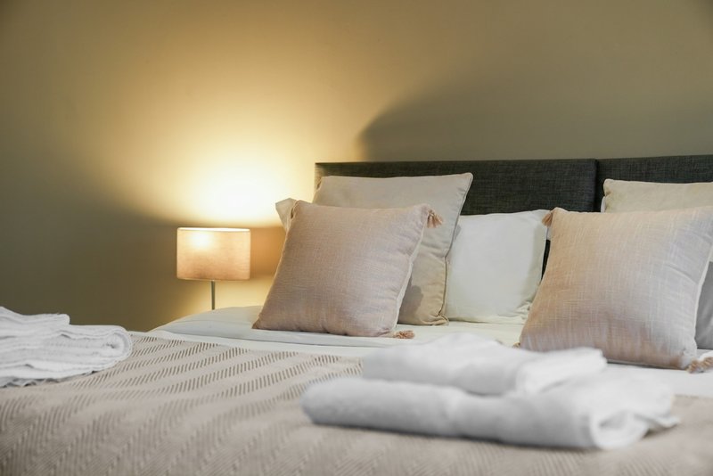 Bedroom with double bed, decorative pillows, bedside lamp and folded towels