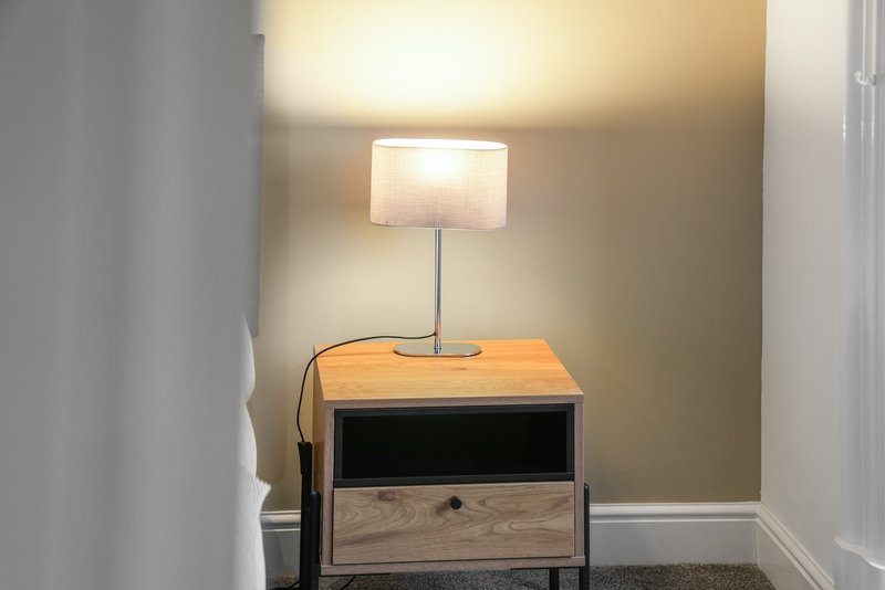 Wooden bedside table with lamp in corner of neutral bedroom