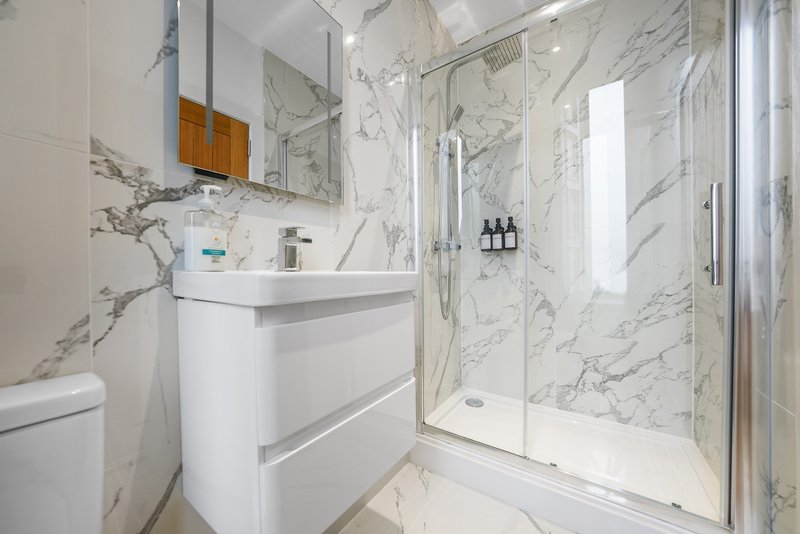 Modern bathroom with marble tiles, white vanity, mirror, shower enclosure and toiletries