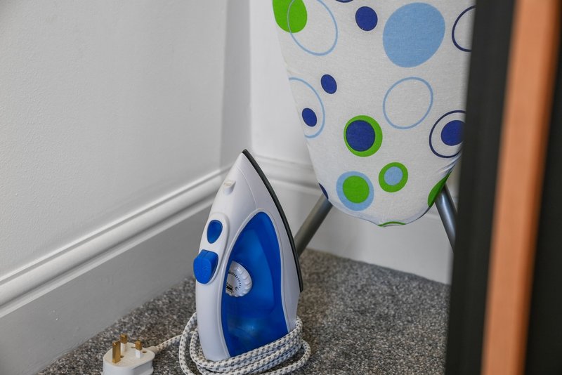 Laundry room corner with iron and colorful ironing board leaning against wall