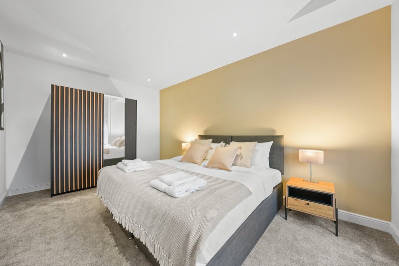 Modern bedroom with double bed, gold accent wall, bedside lamp and wooden nightstand