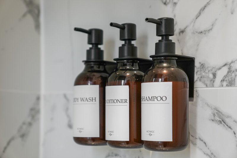 Three amber glass pump bottles with labels for body wash, conditioner and shampoo on marble bathroom shelf