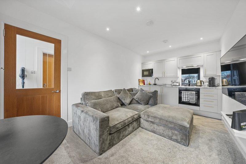 Modern open-plan living area with grey upholstered sofa, round black table and white fitted kitchen
