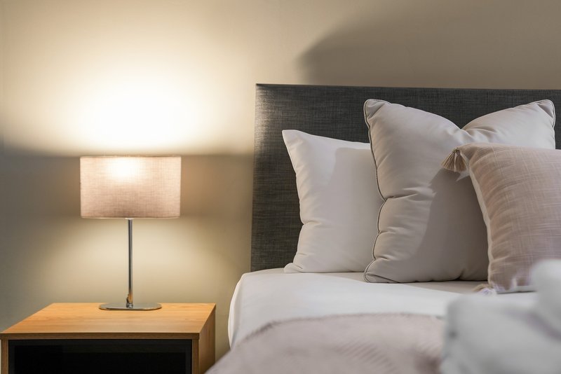 Bedroom with double bed, white pillows, dark headboard, and bedside lamp