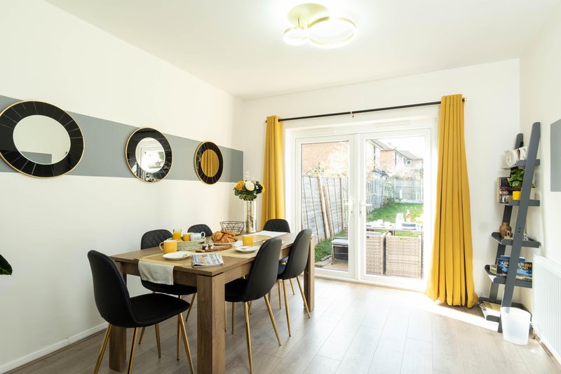 Dining area for 6 people with wooden table, black chairs, decorative wall mirrors and yellow curtains