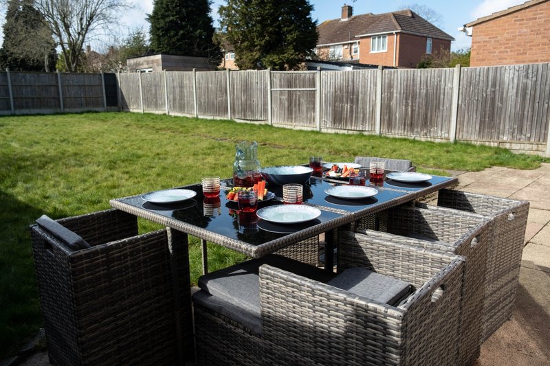 Outdoor garden patio with rattan dining set, place settings, and wooden fence