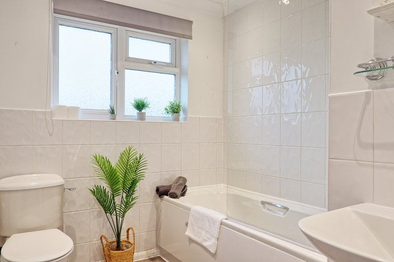 Clean modern bathroom with white tiles, toilet, bathtub, sink and window