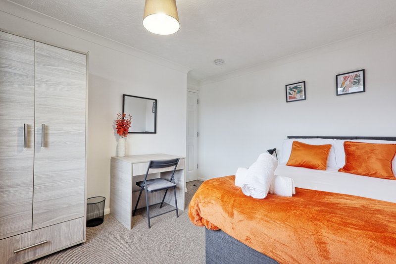 Bright bedroom with orange bedding, desk, chair, wardrobe and ceiling light