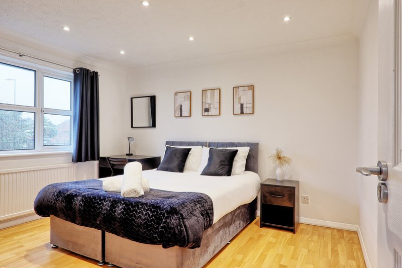 Bright modern bedroom with double bed, wooden floor, blue curtains and wall art