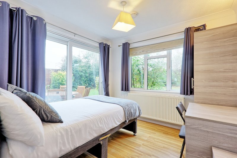 Bright bedroom with double bed, purple curtains, wooden flooring and garden views