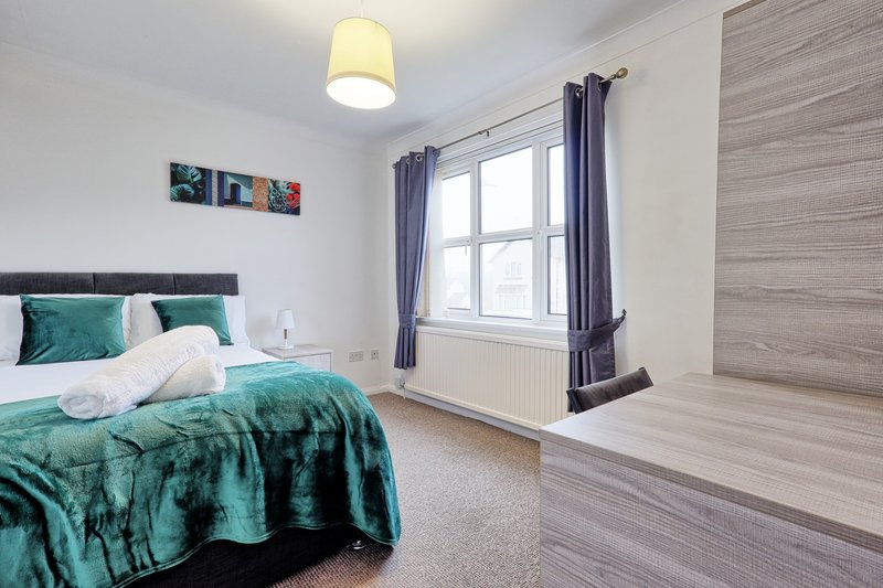 Modern bedroom with double bed, teal bedding, window with curtains, and wooden accent wall