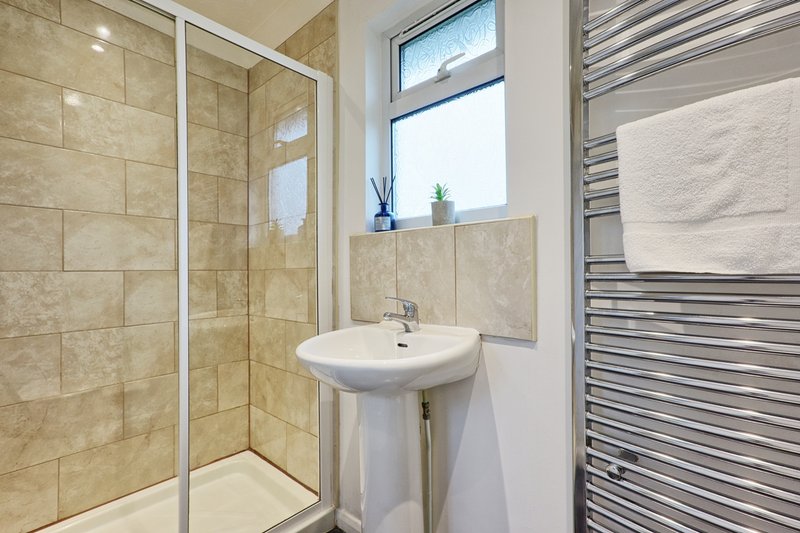 Modern bathroom with walk-in shower, pedestal sink, heated towel rail and window