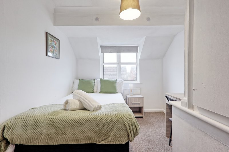 Bright bedroom with double bed, green bedding, window, pendant light and desk area