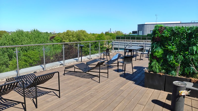 Rooftop terrace with wooden decking, black seating, metal railings and green plants