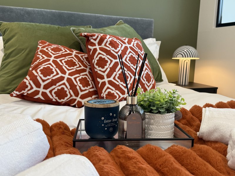 Bedroom with styled bed, patterned pillows, potted plant, and bedside lamp