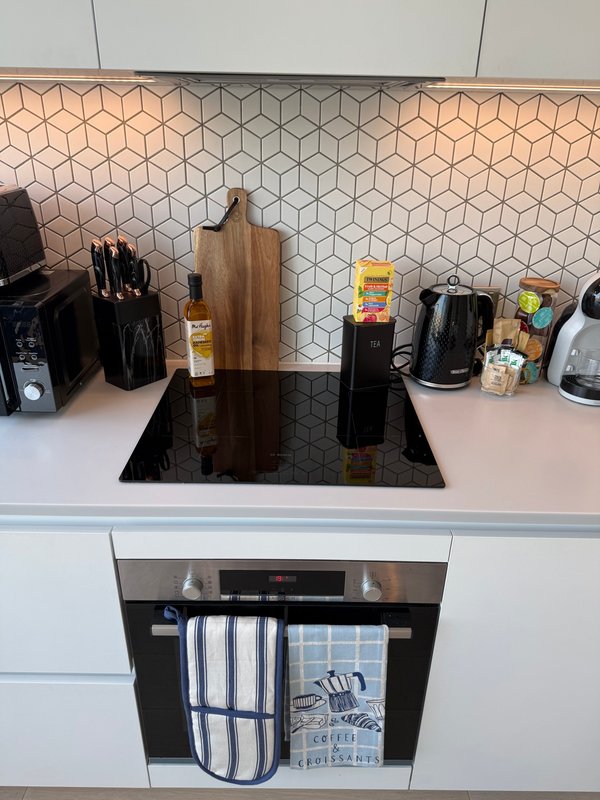 Modern kitchen countertop with cooktop, geometric backsplash tile, and various small appliances and kitchen utensils