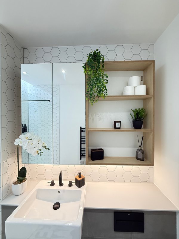 Modern bathroom with white hexagonal tiles, sink, mirror cabinet, wooden shelving, and decorative plants