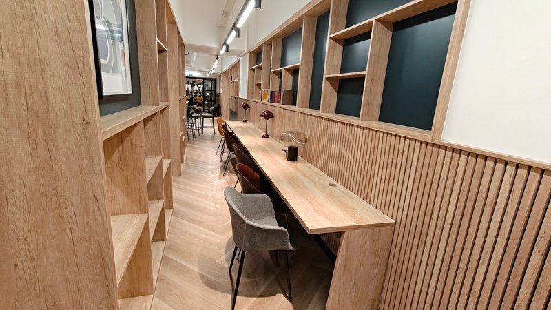 Modern workspace hallway with wooden desks, chairs, shelving units and pendant lighting