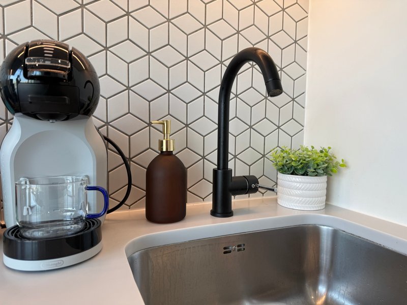 Modern kitchen counter with coffee maker, black faucet, stainless steel sink and geometric tile backsplash