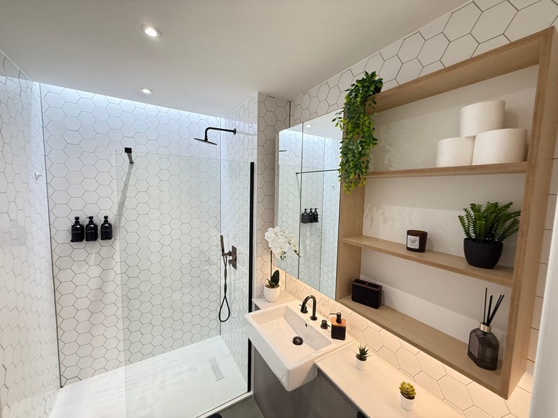 Modern bathroom with walk-in shower, white hexagonal tiles, wooden shelving and vanity sink