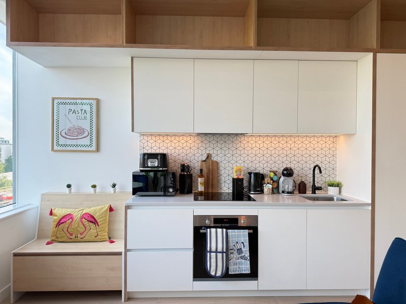 Modern kitchenette with white cabinetry, geometric backsplash, integrated appliances and wooden seating nook