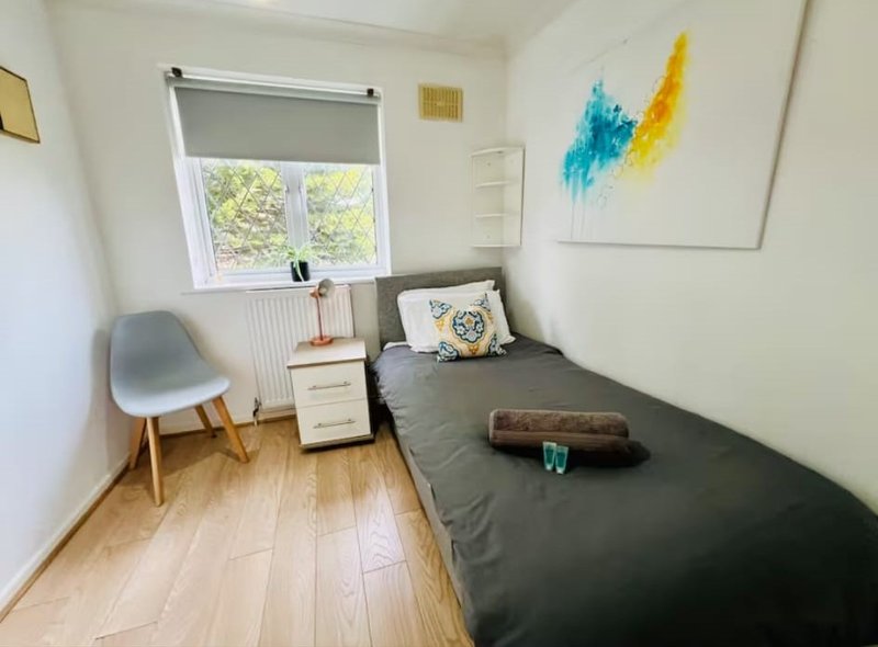 Bright bedroom with single bed, wooden floor, chair, window and wall art