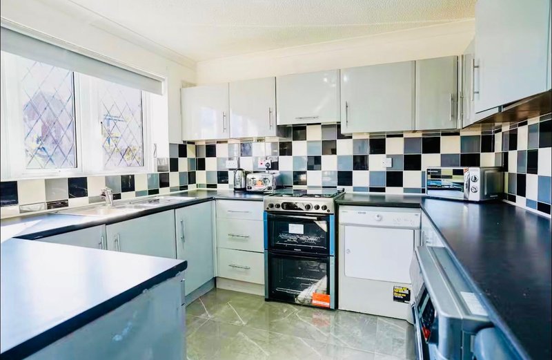 Kitchen with white cabinets, black and white tile backsplash, black countertops and appliances