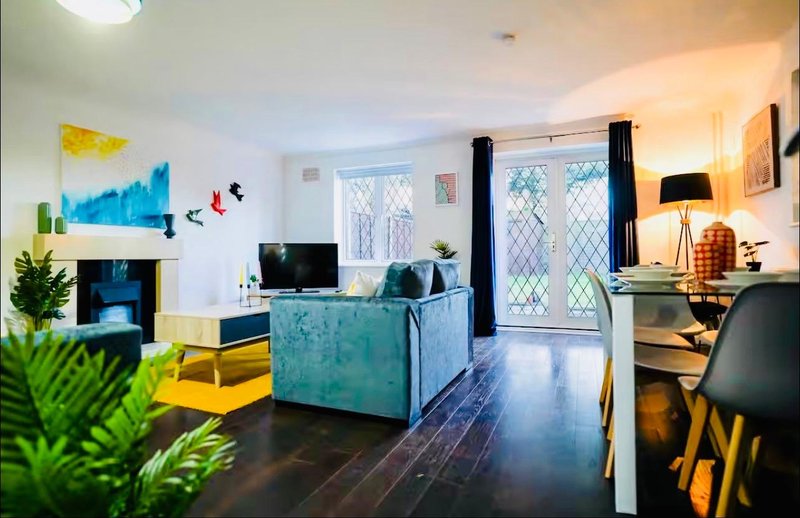 Modern living room with turquoise sofa, TV unit, artwork, plants and patio doors