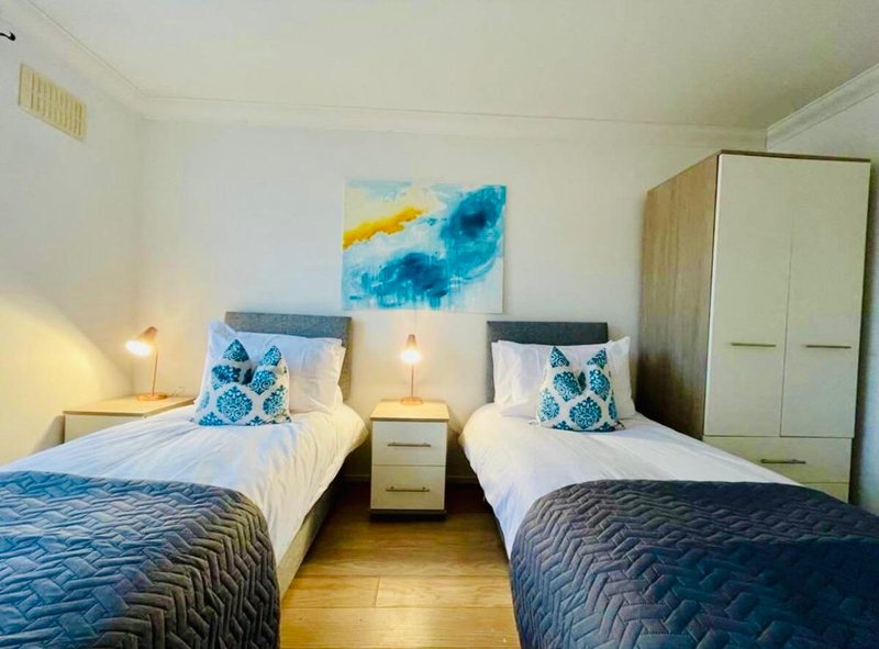 Bedroom with two single beds, blue patterned bedspreads, decorative cushions and abstract wall art