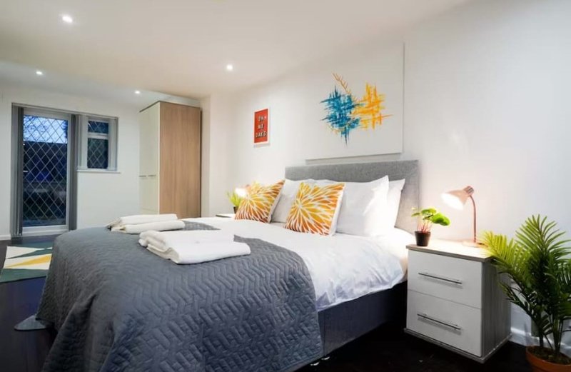 Modern bedroom with double bed, gray headboard, yellow patterned cushions, bedside table with plant and lamp